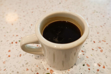 close up of black coffee in a white mug cup on a white mosaic pattern table