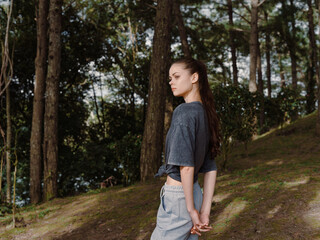 Fototapeta premium Thoughtful young woman standing in a serene forest setting, wearing a relaxed outfit, looking contemplative and embracing nature s tranquility
