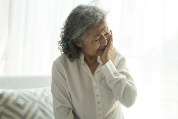 Senior asian woman experiencing tooth pain, holding his cheek with pained expression, discomfort...