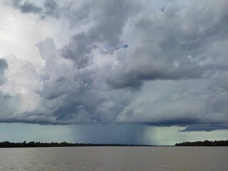 A view of thick clouds pouring heavy rain over the land and river below, creating a misty atmosphere.