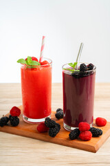 vertical photo of vibrant raspberry smoothies and blackberry smoothies and mint leaves on wooden table with white background