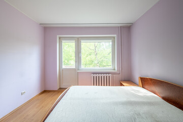 Fototapeta premium Minimalism Bedroom Interior. Wardrobe and Window in Background. Apartment is Ready for the Rent. White Heater. Old Soviet Style Room Interior. Home Interior. Pink Walls. Closed Doors to Balcony