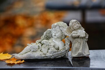 Fototapeta premium Sleeping angel figure on a grave in autumn with fallen leaves.