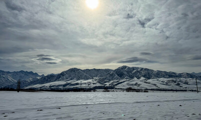 The sun breaks through the clouds over snow-covered mountains in Kyrgyzstan. A beautiful sight for winter tourism and mountain adventures.