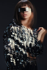 A woman in a sparkling sequinned dress and sunglasses stands against a black background, exuding...
