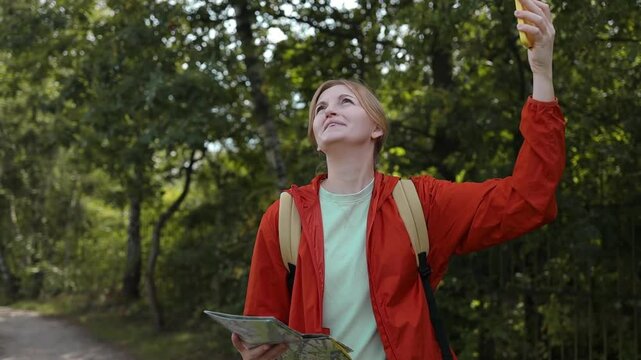 Caucasian girl with backpack using GPS smartphone. Woman walks through the forest and types a message on her smartphone. No connection in the forest. Single tourist using a smartphone. 