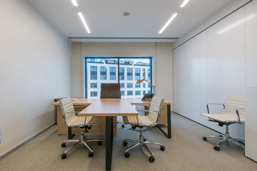 The workspace features a minimalist office layout with a large desk, comfortable chairs, and a bright window that offers a view of the city, enhancing the professional atmosphere