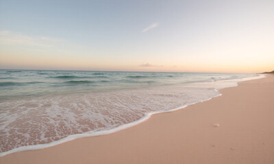 A breathtaking beach scene at sunrise with soft golden light illuminating the waves as they gently lap against the  shore