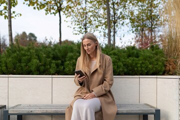 A businesswoman checks her phone while sitting on a bench near a business center