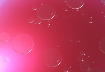 Una toma de cerca de varias burbujas de agua y aceite en movimiento en un fondo de color rosado