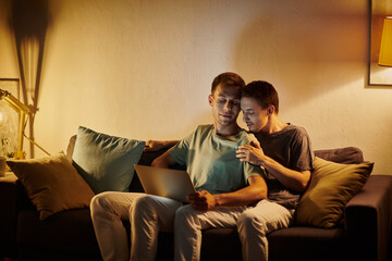 Obraz premium Two men enjoy a warm moment together while using a laptop on the couch.