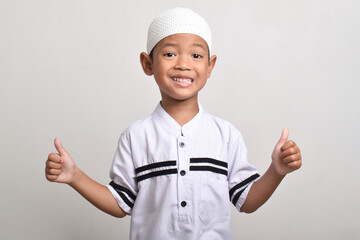 Portrait of a Muslim Asian boy smiling happily and giving a thumbs up isolated on a white background.