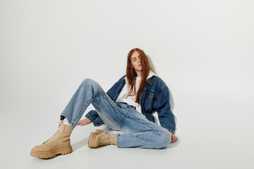 The teenage boy with long red hair poses effortlessly in a denim outfit, exuding confidence and...