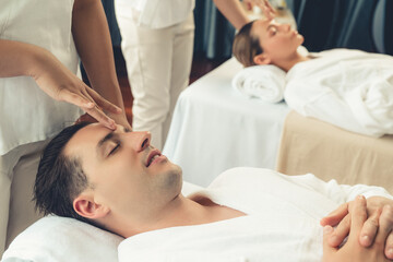 Caucasian couple enjoying relaxing anti-stress head massage and pampering facial beauty skin recreation leisure in dayspa modern light ambient at luxury resort or hotel spa salon. Quiescent