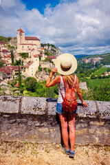 Woman tourist with hat and backpack looking at one of beautiful village in France, Saint cirq...