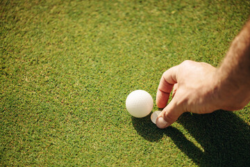 Close-up of a man's hand setting up a golf ball and moving the ball marker for the perfect shot