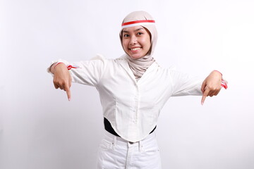 Young asian muslim woman with red white ribbon celebrating Indonesia independence day while pointing down