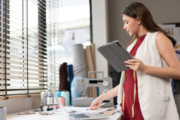 FYoung fashion designer using digital tablet checking customer order and browsing for concept idea...