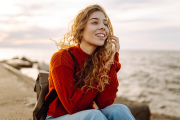 Young woman enjoying a breezy day near a vibrant red lighthouse.  Autumn sunset at a background....