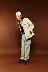 A teenage boy with striking red hair is stylishly dressed, smiling broadly in a studio setting.