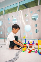 Little kindergaretn boy enjoying building colorful toy block in school