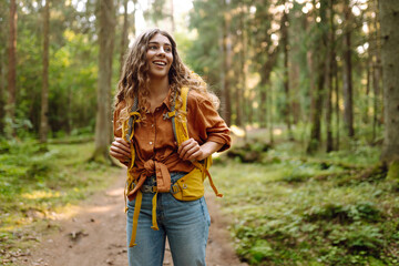 Tourist woman hiking alone in thick autumn forest. Stylish female looks for pathway among large...