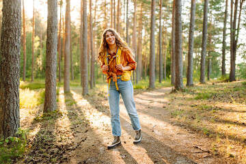 Tourist woman hiking alone in thick autumn forest. Stylish female looks for pathway among large trees. Active lifestyle.