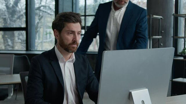 Caucasian senior man professional mentor checking male employee in office teach intern training new worker consult customer explain online business service computer corporate software looking screen