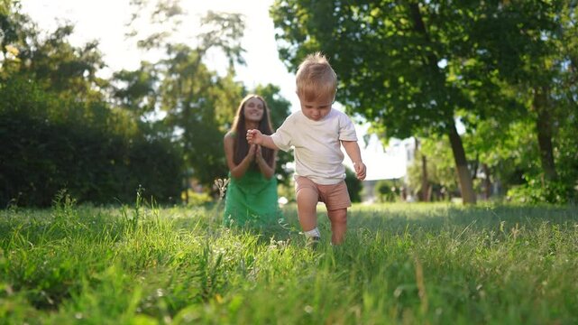 Happy family. Mother and son take their first steps. Child mother step concept. A baby is taking the first steps in the grass. Mom and baby taking first lifestyle steps in the grass.