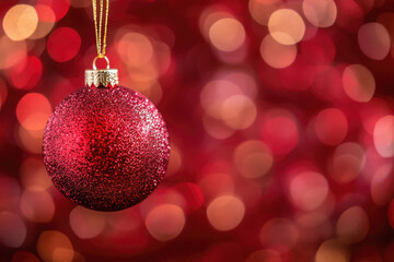 Fototapeta premium A red and gold ornament hangs from a string. The ornament is a Christmas ball. The background is blurry and red