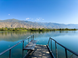 Fototapeta premium A wooden pier on Issyk-Kul lake with a view of the mountains. A beautiful spot for relaxation and enjoying the natural landscapes of Kyrgyzstan