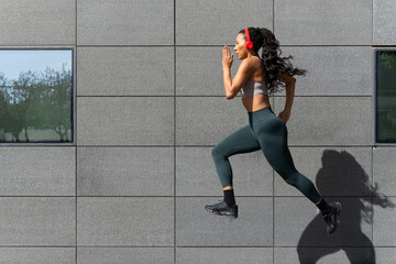 Young latin american woman running outdoors wearing headphones