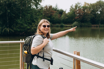 Fototapeta premium Stylish hipster woman wearing backpack pointing finger, relaxing in nature. Travel and wanderlust concept. Amazing chill moment.