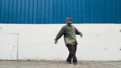 Hipster dancing b-boy foot step at street with blue wall. Asian break dancer practice street dance while stretch arms. Hip hop choreographer perform energetic dance. Outdoor sport 2024. Hiphop.
