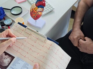 Doctor cardiologist examining electrocardiogram on background of artificial model of heart.