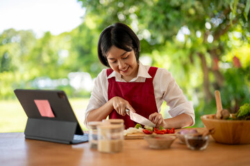 Asian woman following recipe on digital tablet cooking healthy food