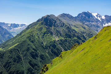 Naklejka premium Scenic views on snowy mountain peaks and valley at summer. Green meadows and forests, slopes, hilly countryside, blue sky with clouds. Beautiful landscape, travel background, wallpapers and banner.
