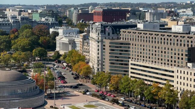 A aerial view of Washington DC cityscape with White House, US Treasury, government buildings, trees, and cars. The view includes a street, and multiple trees with fall foliage.