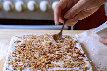 Woman's hand sprinkling top of cake. Decorating top of cake with crumbs of mixture of chocolate, nuts and caramel. Close-up. Decorating top of Napoleon cake.