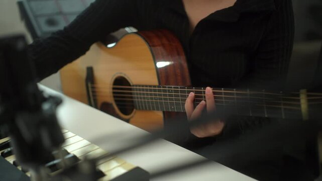 Close up hand of young musician woman playing guitar for songwriting using tablet and music instrument in digital recording home studio, a composer female wearing headphone mastering music soundtrack.