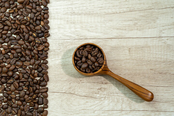 Roasted coffee beans on wooden background and inside a wooden measuring cup
