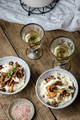 risotto with gum chanterelle mushrooms and two glasses of wine on a wooden table