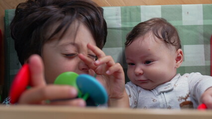 Young boy wipes his nose with his hand, indicating a runny nose, while lying beside the baby on the mat