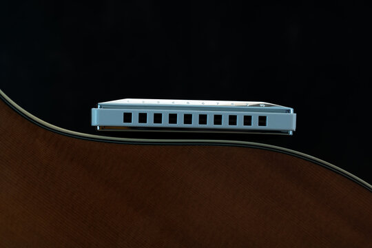 Macro close up diatonic harmonica lying on side of guitar body showing the curve of the guitar body