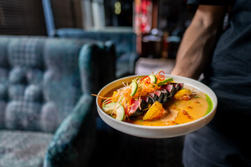 A person holding a vibrant dish with colorful vegetables and sauce, perfect for culinary or lifestyle themes. The close-up shot highlights the freshness and appeal of the ingredients