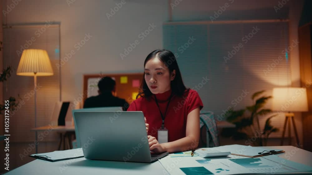 Poster young asian manager working late in the office, focusing intently on her laptop while typing on the 