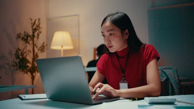Young professional working late in the office, focusing on her laptop while typing on the keyboard. The atmosphere reflects dedication and ambition in a modern corporate environment