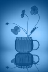 creative composition still life with transparent mug and tea, with flower in fog, concept summer, spring, bloom, tenderness, birthday card, holiday, blue toned