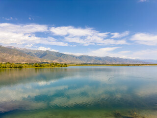 Obraz premium A quiet mountain lake Issyk-Kul, surrounded by green valleys and majestic mountains. The perfect spot for tourism and peaceful relaxation in Kyrgyzstan.