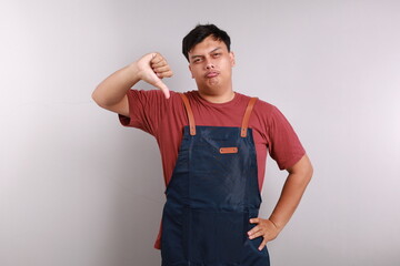 Moody unsatisfied asian man wearing blue apron, disliking bad restaurant food smirking displeased,...